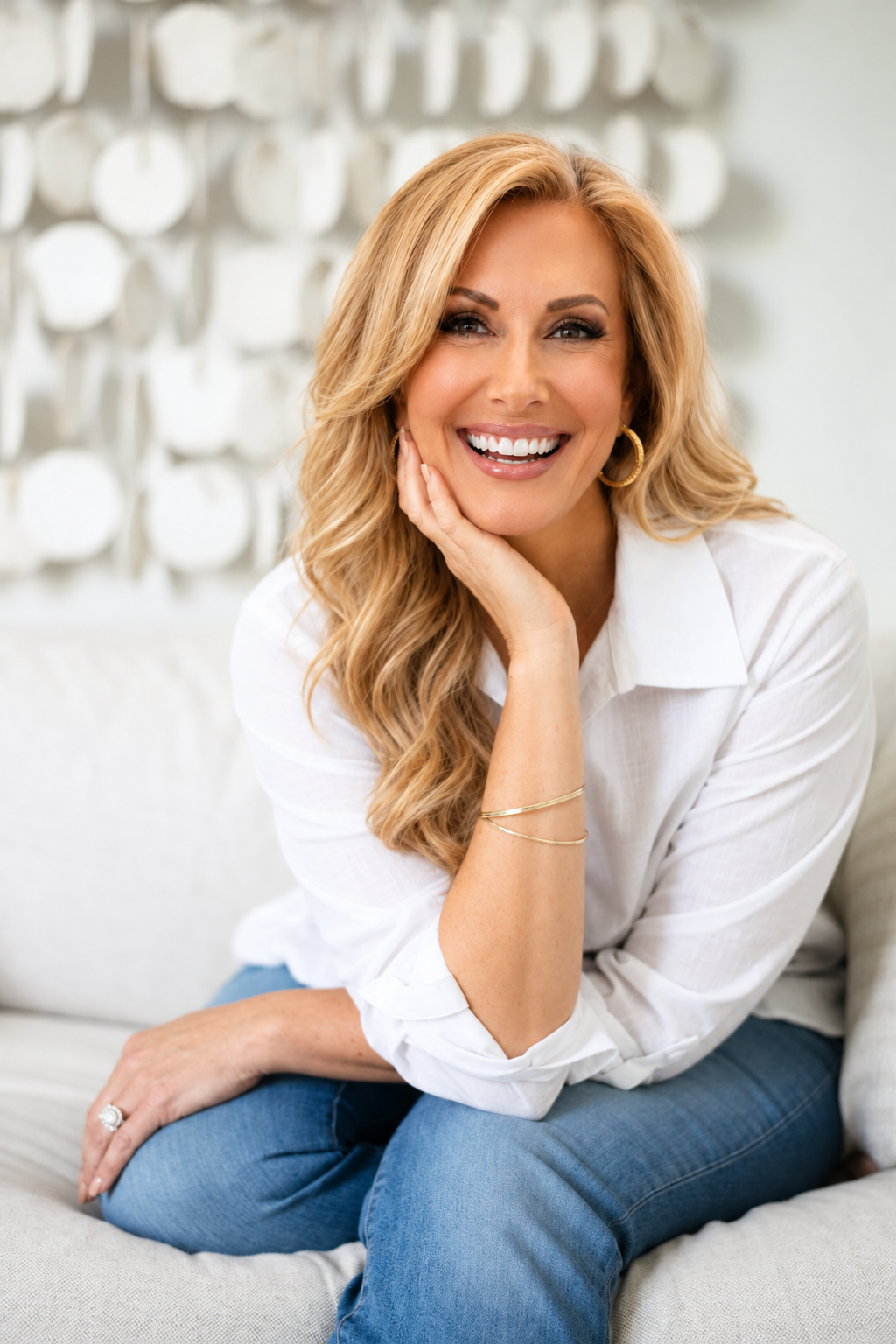 Dr. Tammy Tucker, founder of Hormone Bliss, seated on a light sofa in a white shirt and jeans, smiling with her hand resting against her cheek