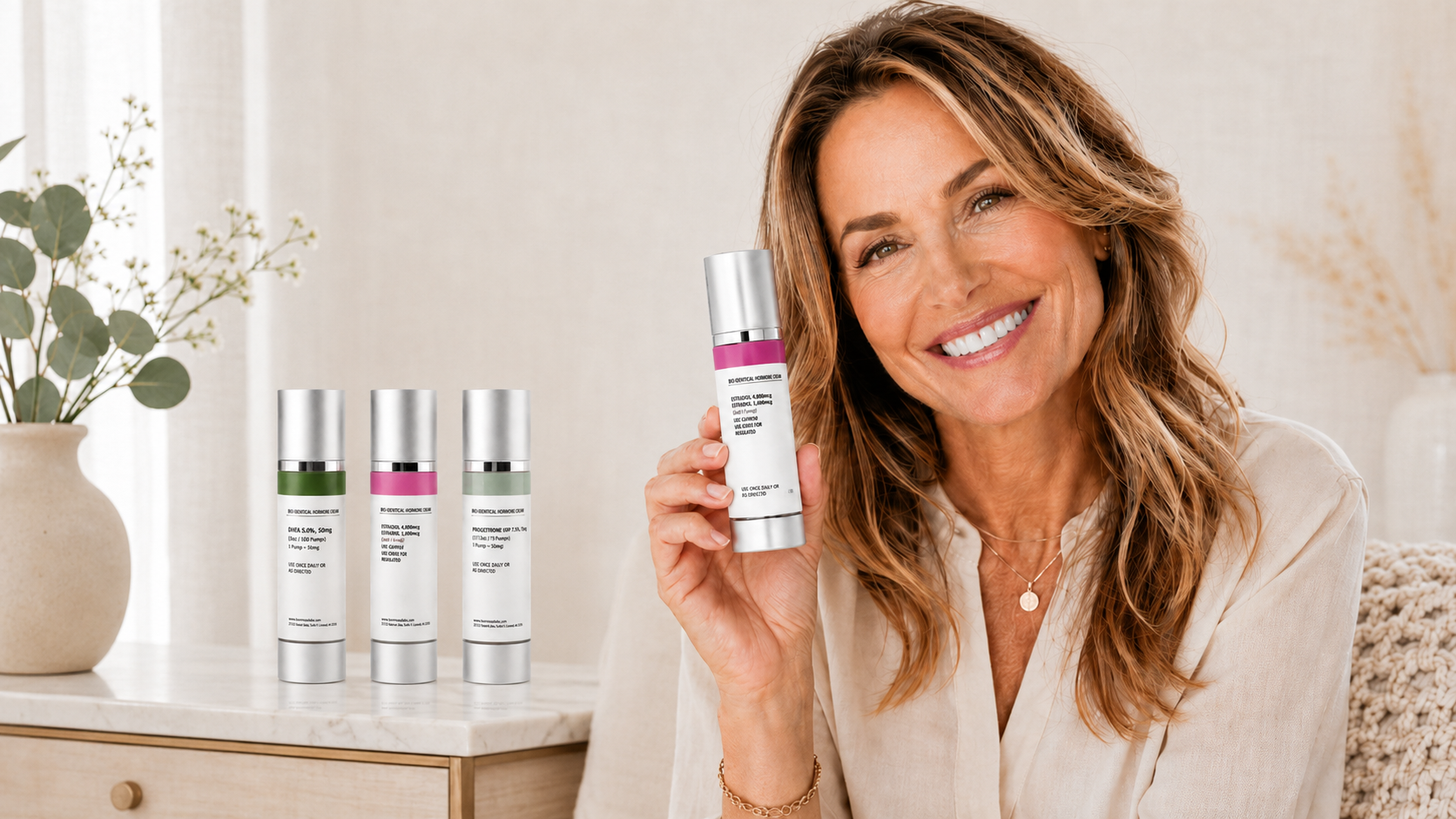 Smiling woman holding a Hormone Bliss bio-identical topical cream bottle, with three additional cream bottles arranged on a marble table beside her.